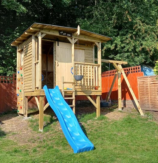 The play house sits on stilts with a slide, swing and clibing wall